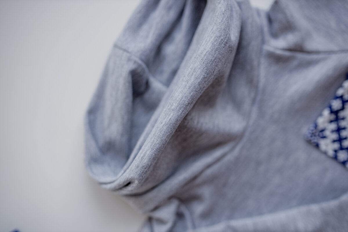 Džemperis gaiši pelēkā krāsā ar mazu zilo latvisko kabatu