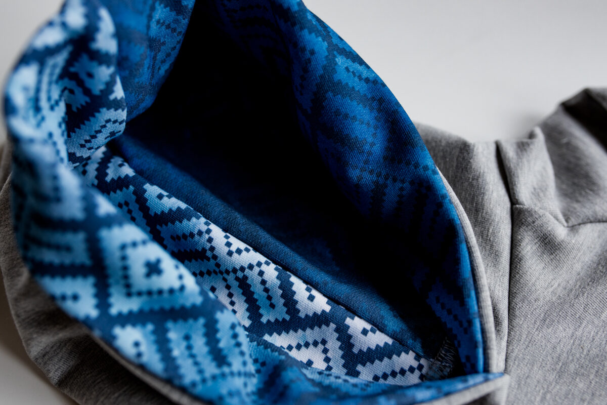 Džemperis gaiši pelēkā krāsā ar zilo rakstu kapuci